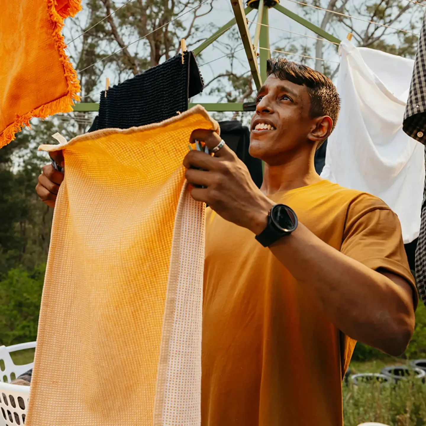 Support worker hangs an orange towel on the Hills Hoist clothesline in the backyard.