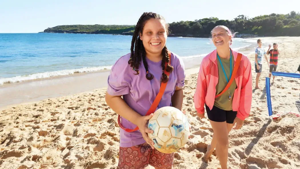 A client and her support worker play volleyball on the beach together.