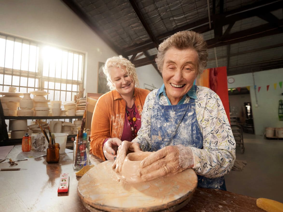Support worker and client throwing clay on a potter's wheel together.
