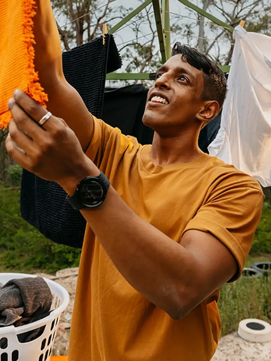 Support worker hangs an orange towel on the Hills Hoist clothesline in the backyard.