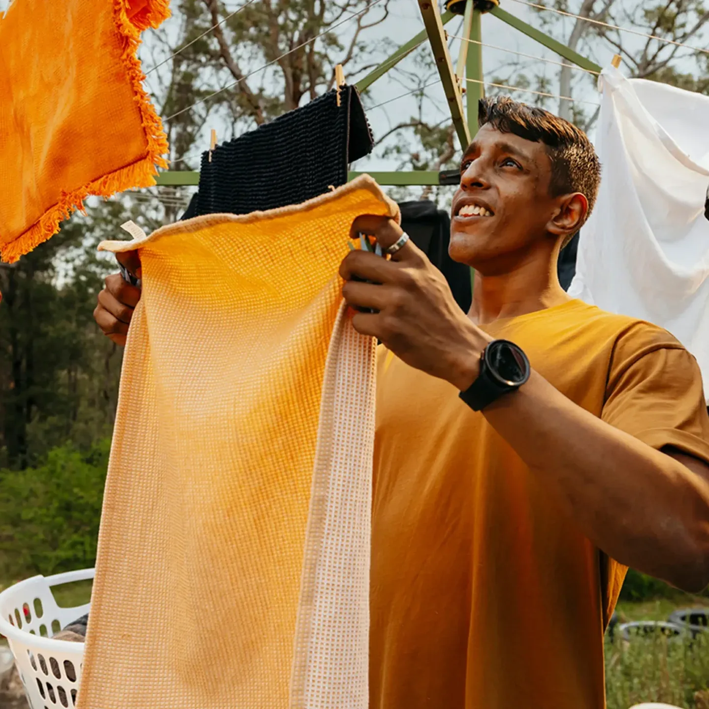 Support worker hangs an orange towel on the Hills Hoist clothesline in the backyard.