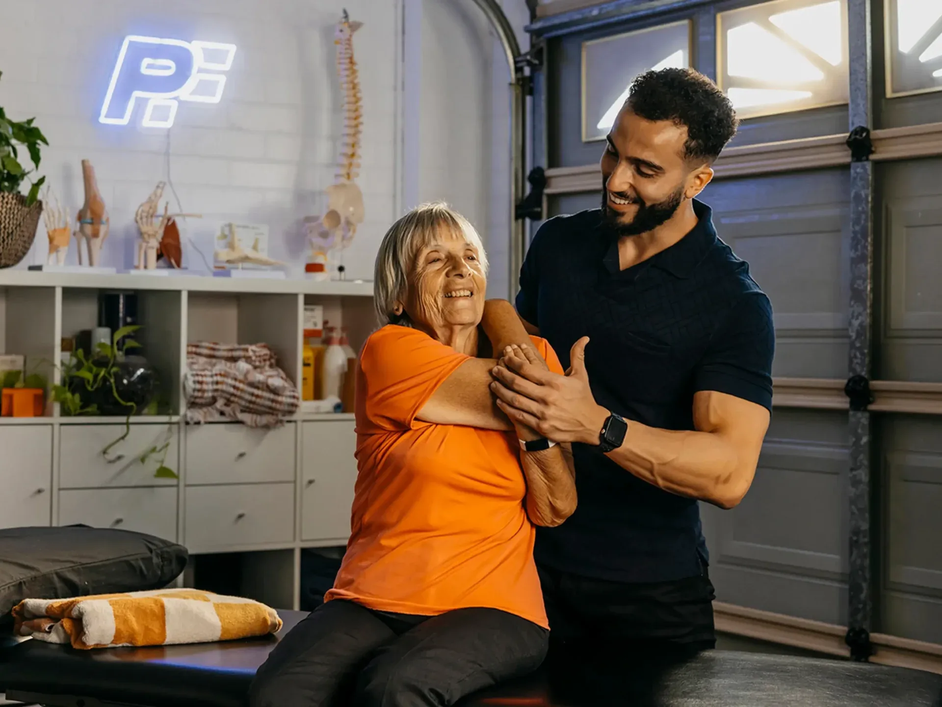 Physiotherapist supports older client’s arm and back during arm stretch over the shoulder.