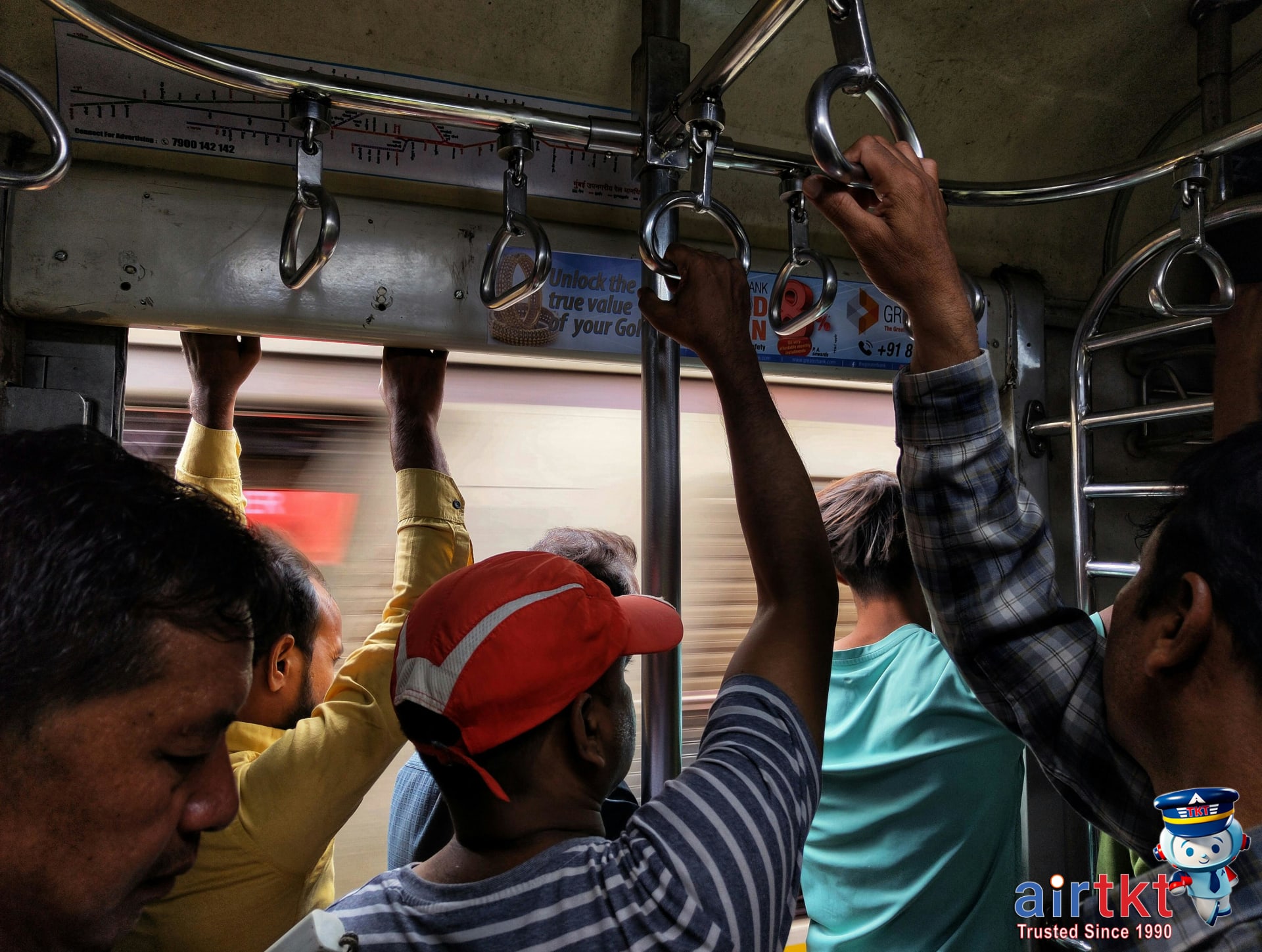 Passengers standing and holding handles inside a busy Mumbai local train.