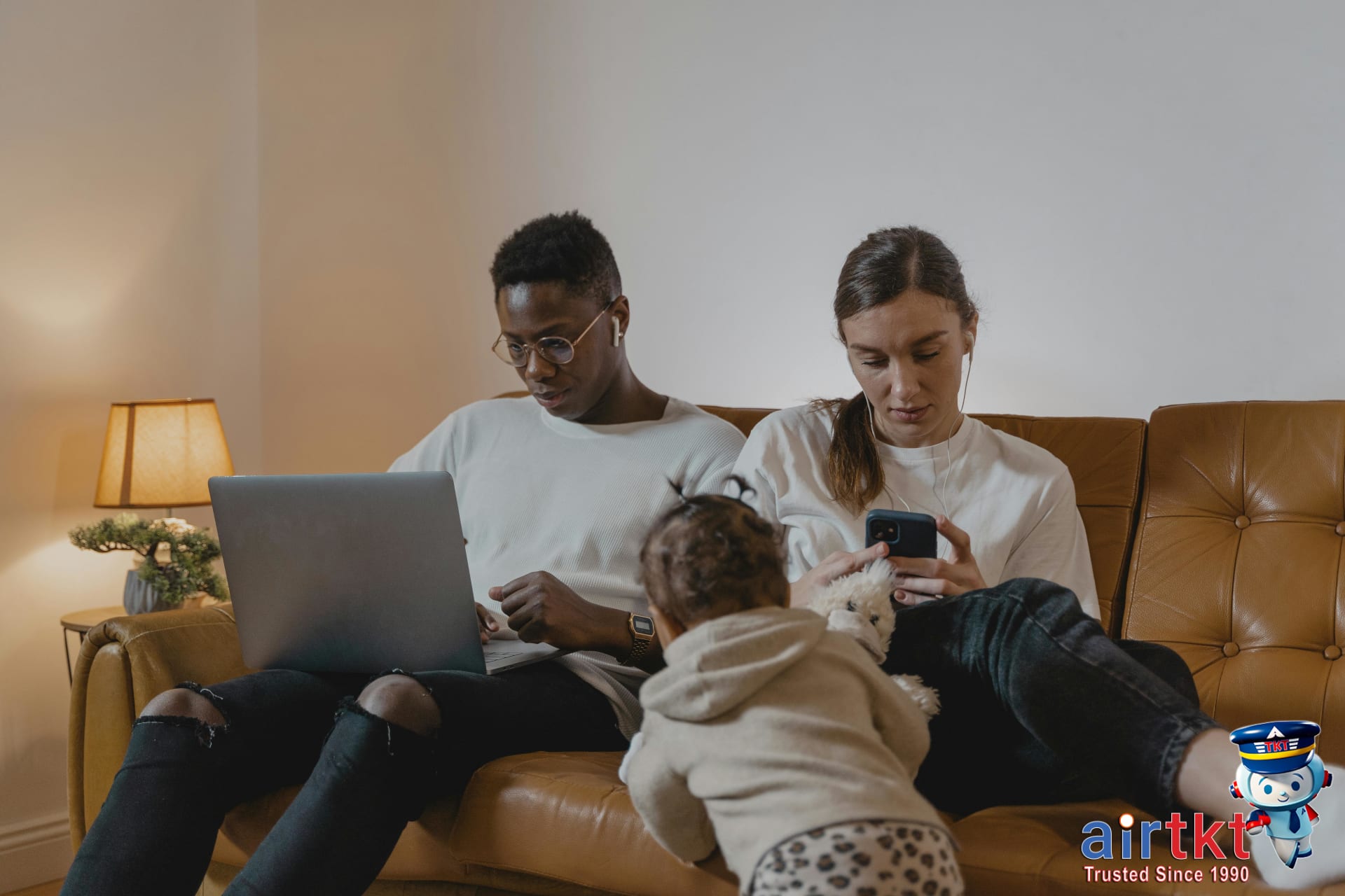 Family sitting on couch using laptop and phone with toddler playing nearby planning April spring break budget