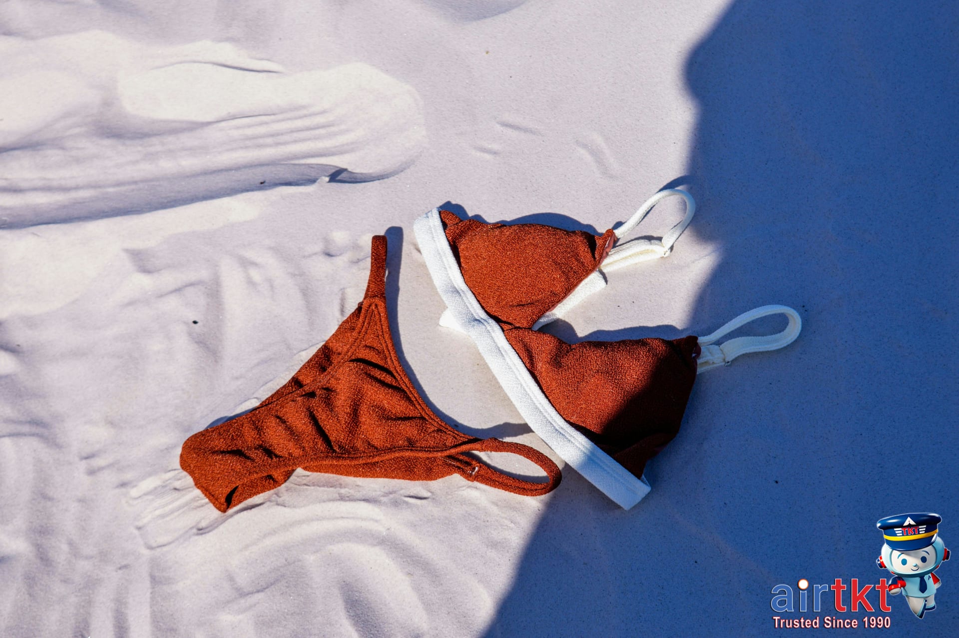 Red bikini swimwear laid out on beach sand for tropical packing