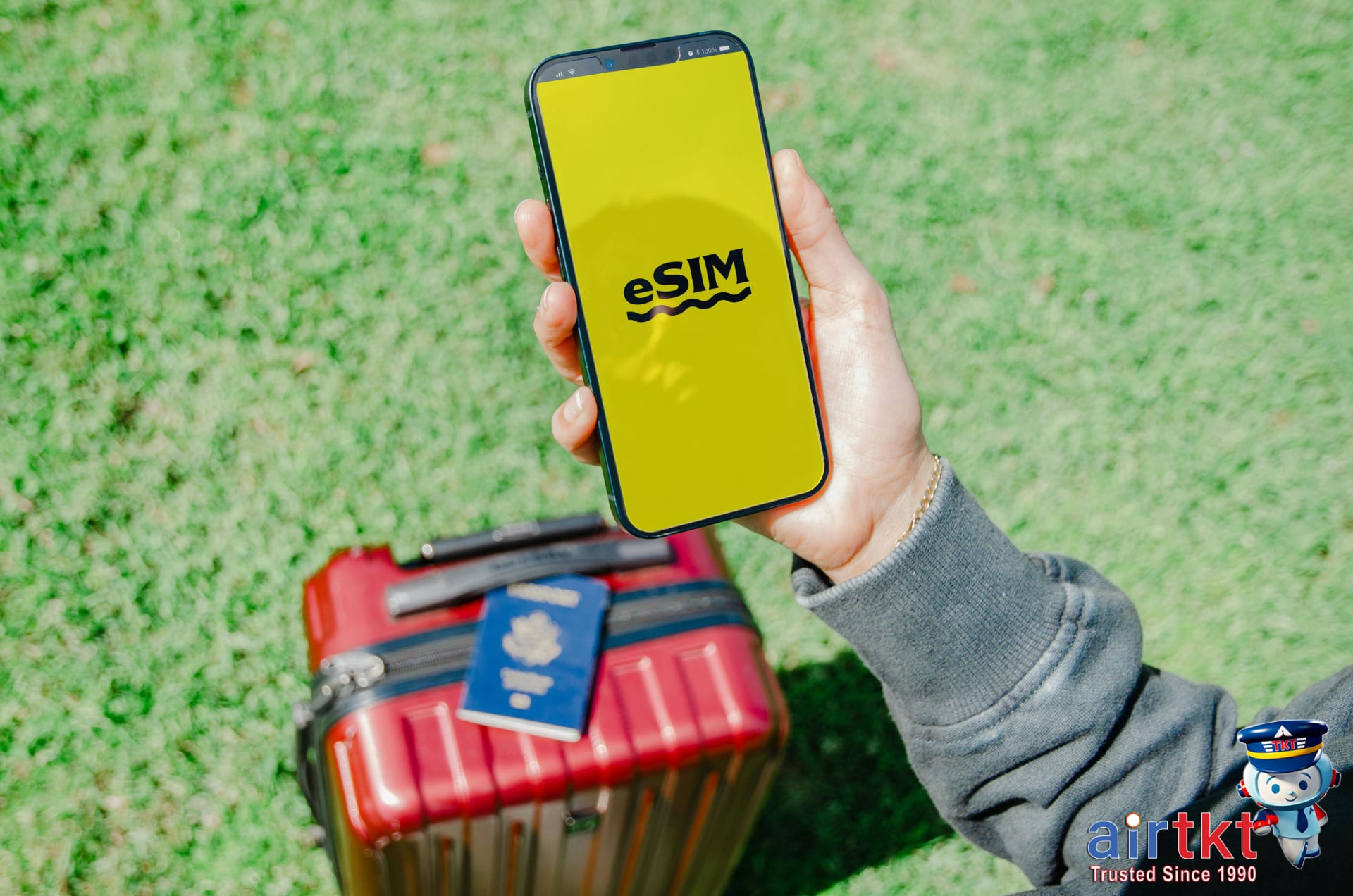 Traveler in Los Angeles holding a smartphone with eSIM near red suitcase