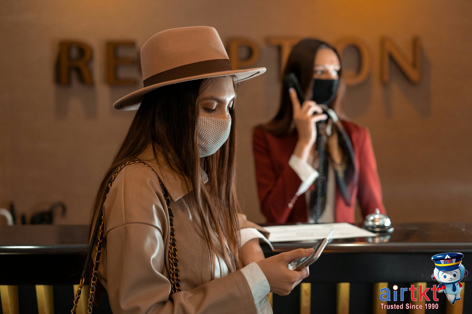 Woman wearing a mask checking her phone at hotel reception comparing cancellation policies