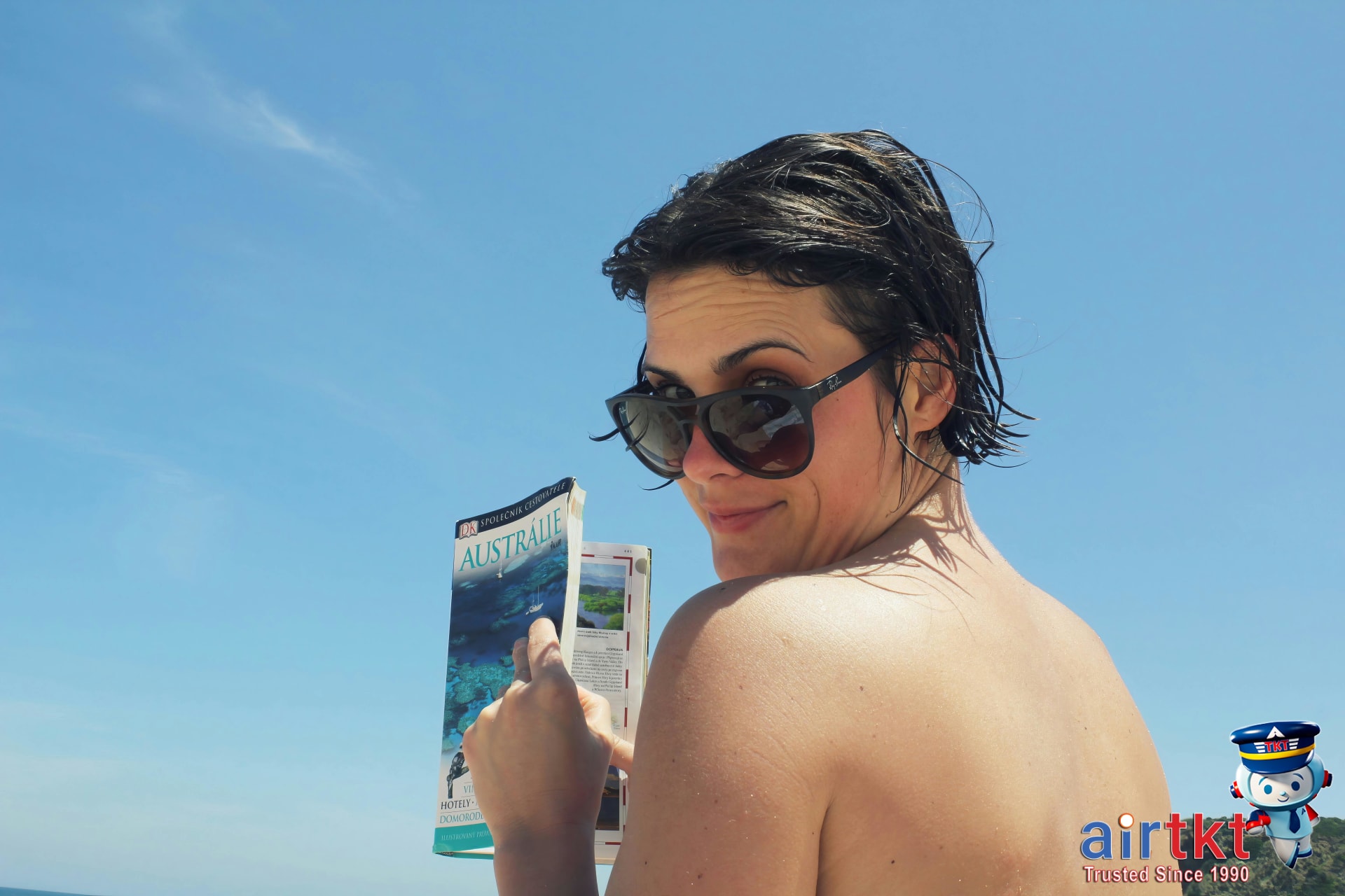 Traveler reading a beach travel FAQ guidebook on a sunny Mediterranean coast
