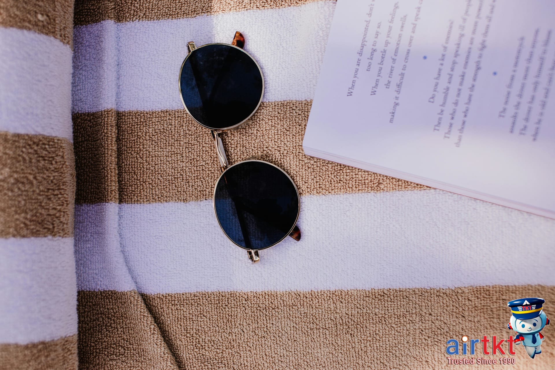 Travel budget essentials including sunglasses and guidebook on a beach towel