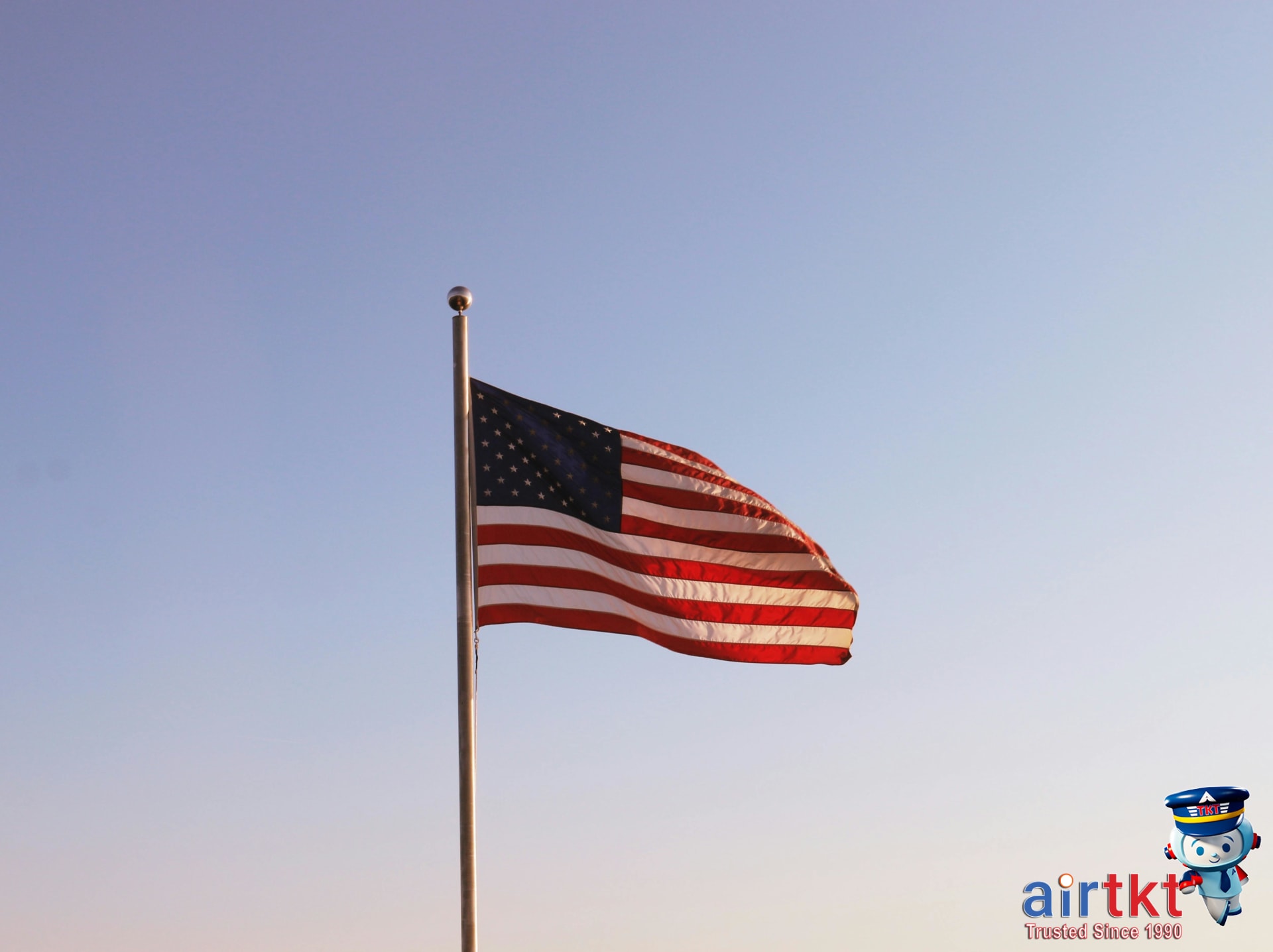 American flag waving symbol for Flag Day travel FAQ against blue sky