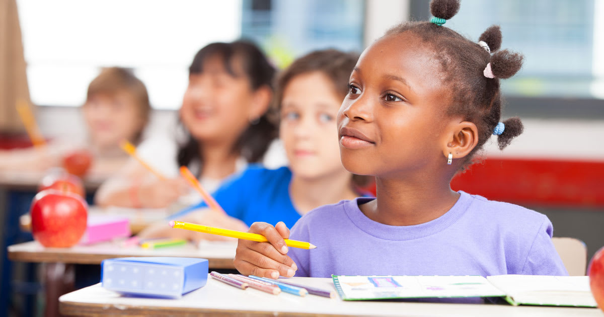 A little girl sitting at her desk in a classroom.