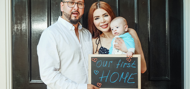 A family showcasing their “our first home” placard