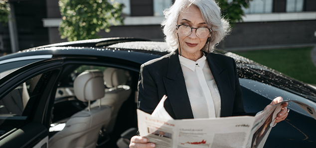 Woman reading newspaper in front of a car