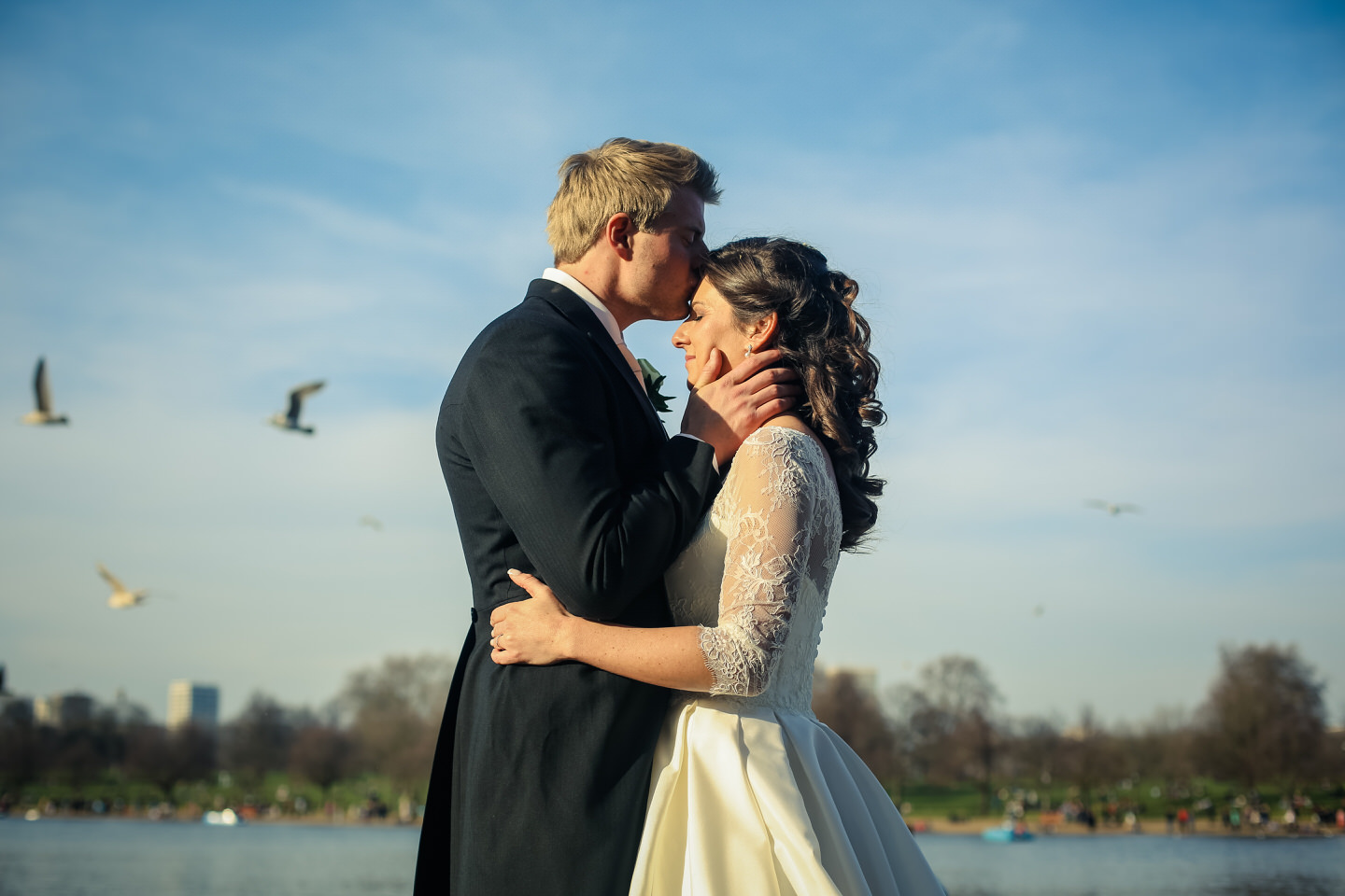 Bridebook.co.uk- groom kissing bride on the forehead by the serpentine lake