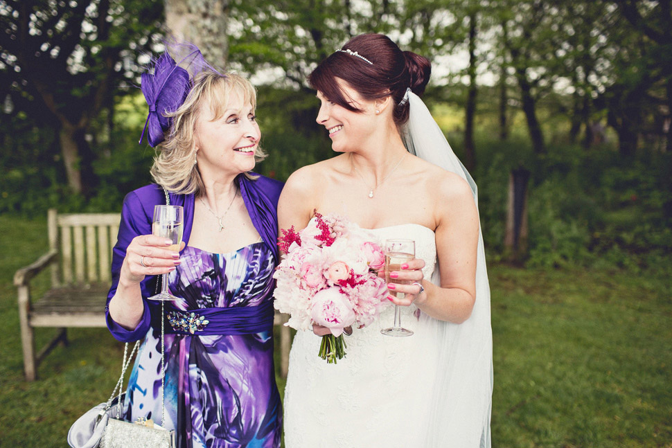 Bridebook.co.uk- mother and bride smiling at each other holding glasses of champagne
