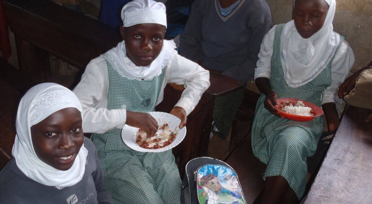 Three Ugandian girls at school eating a lunch of rice and beans