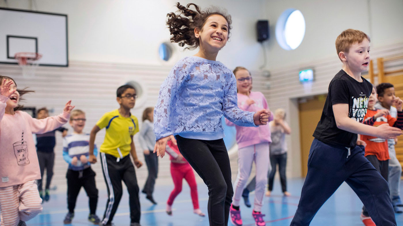 Barn i lågstadieåldern rör på sig tillsammans i en gymnastiksal.