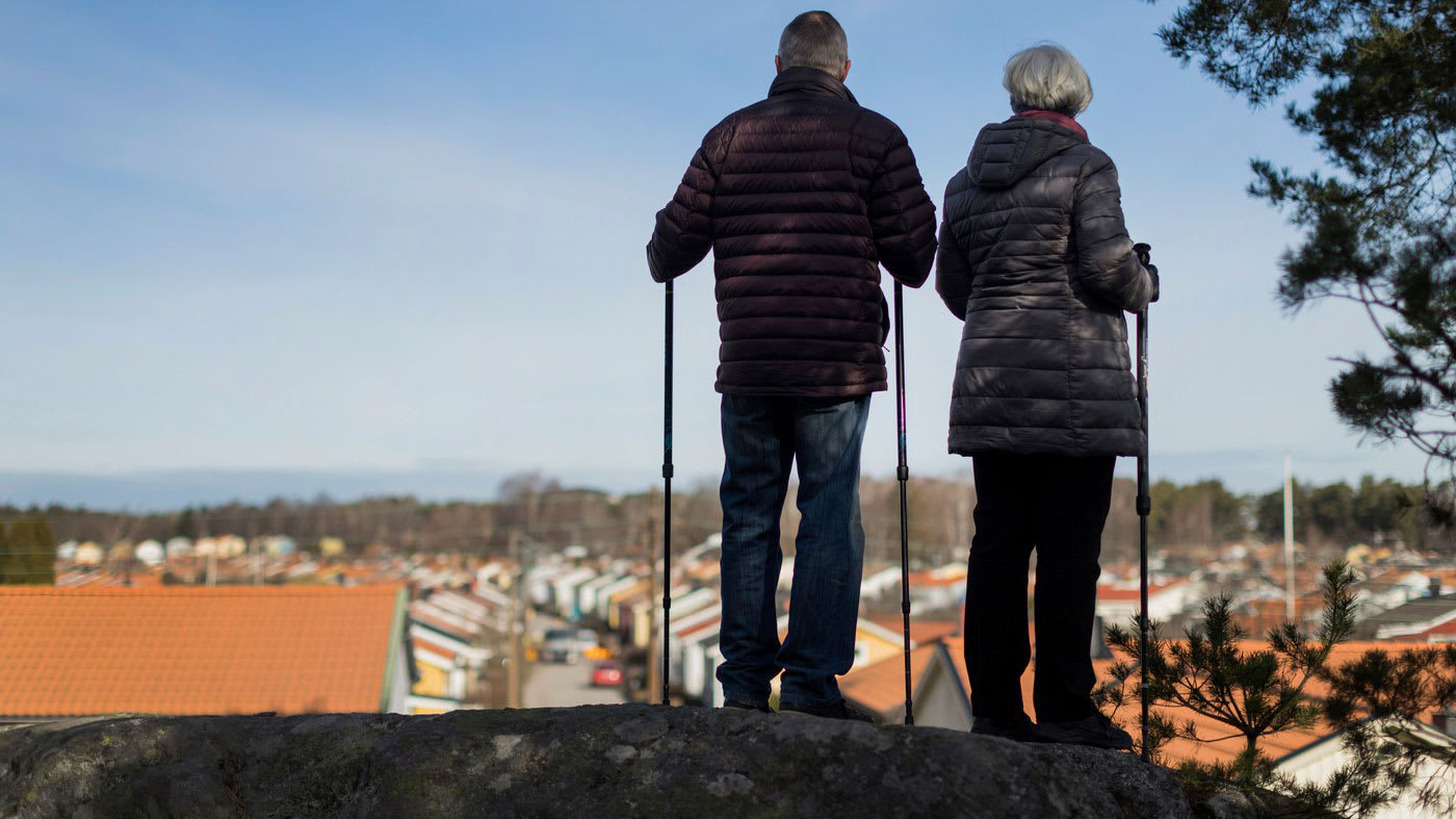 Ett äldre par med gåstavar står bredvid varandra och tittar ut från ett berg