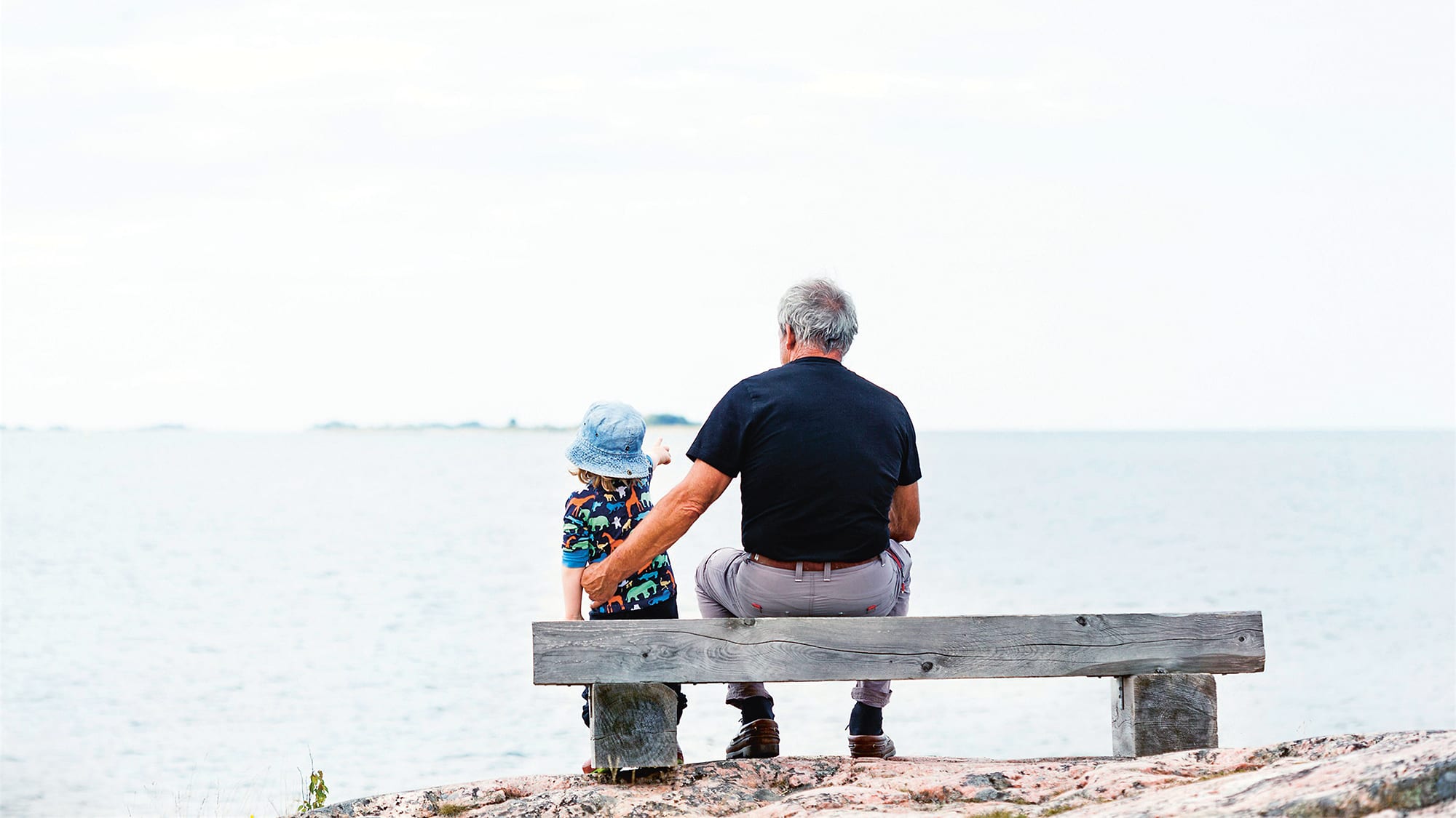 Ett barn och en man sitter på en bänk vid havet