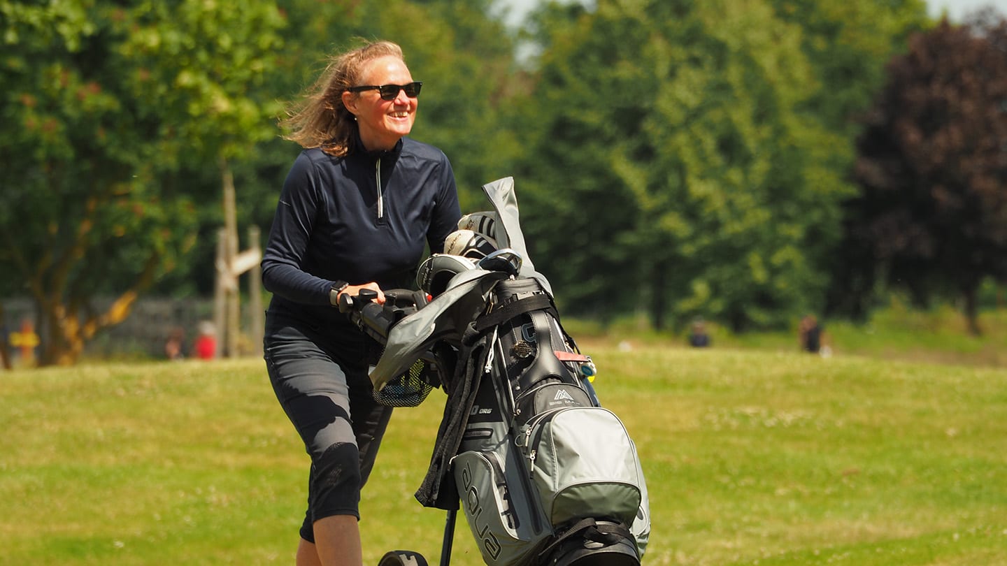 Kvinna drar en golfvagn på golfbanan