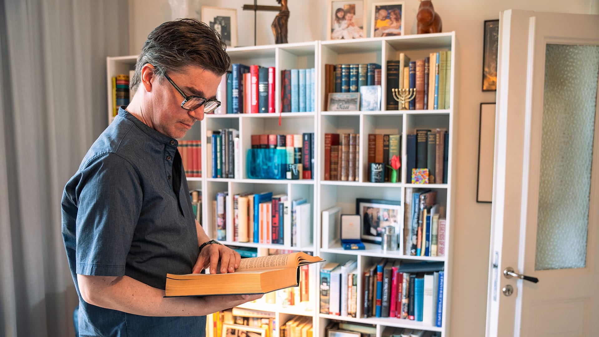 Martin Kragh står vid bokhyllan och håller upp en bok