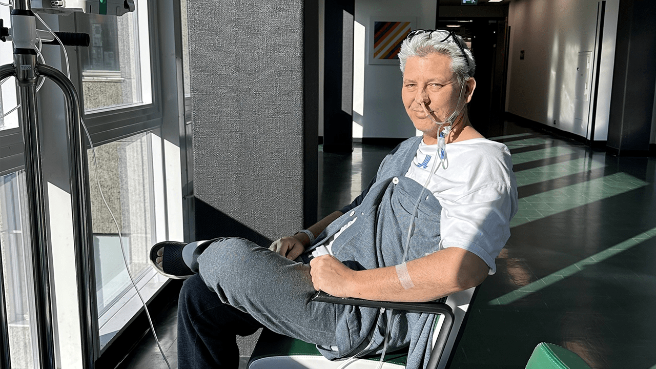 En man som ler vid ett fönster på sjukhuset med en slang i näsan.