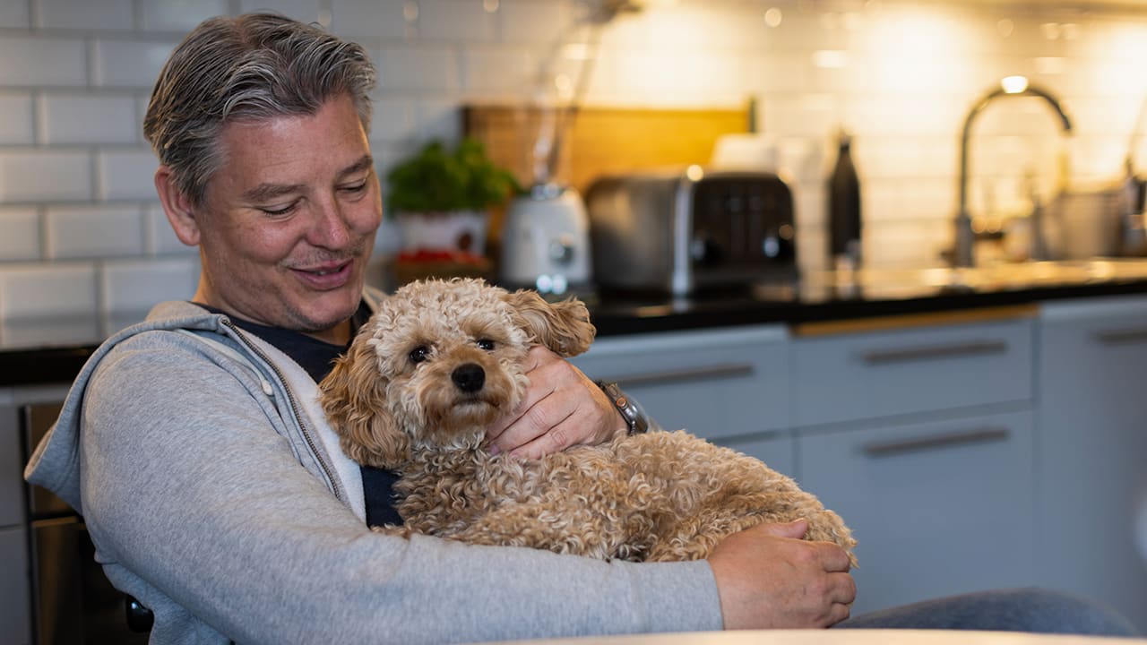 Medelålders man sitter vid köksbordet med sin hund i knäet.