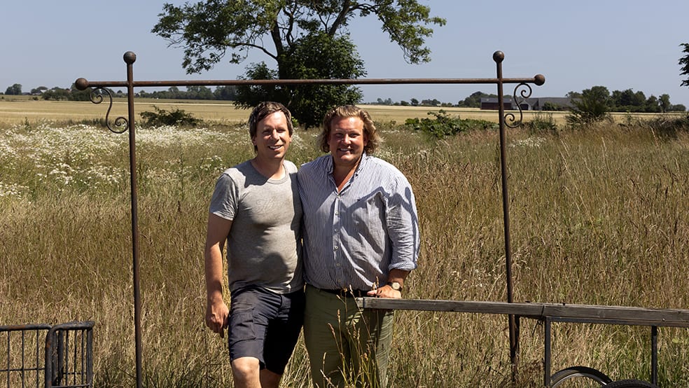 Två medelålders män håller om varandra i skånskt landskap