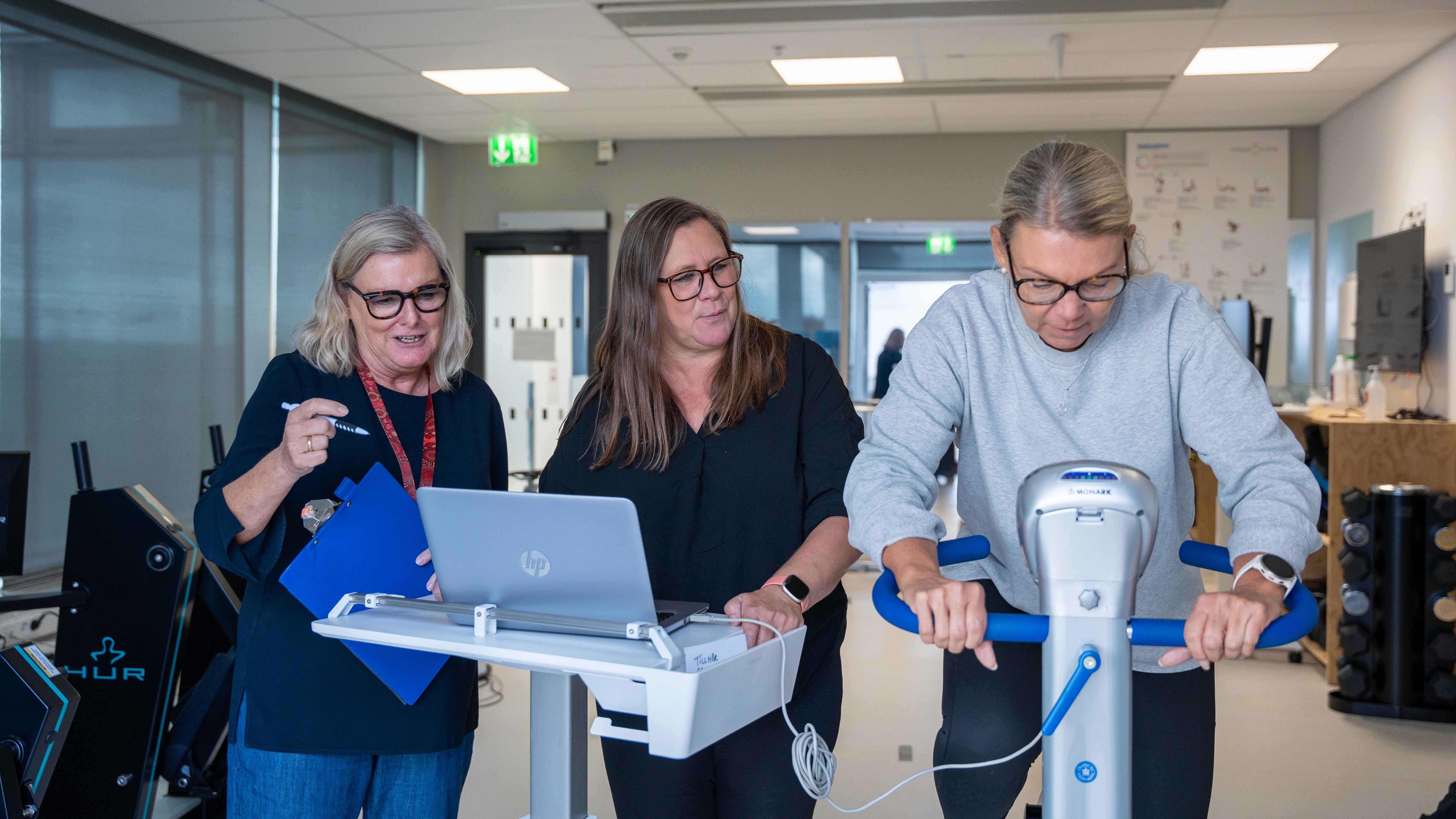 tre personer vid en träningscykel