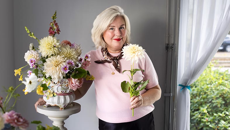 Kvinna i rosa tröja håller vit blomma bredvid blombukett i vas