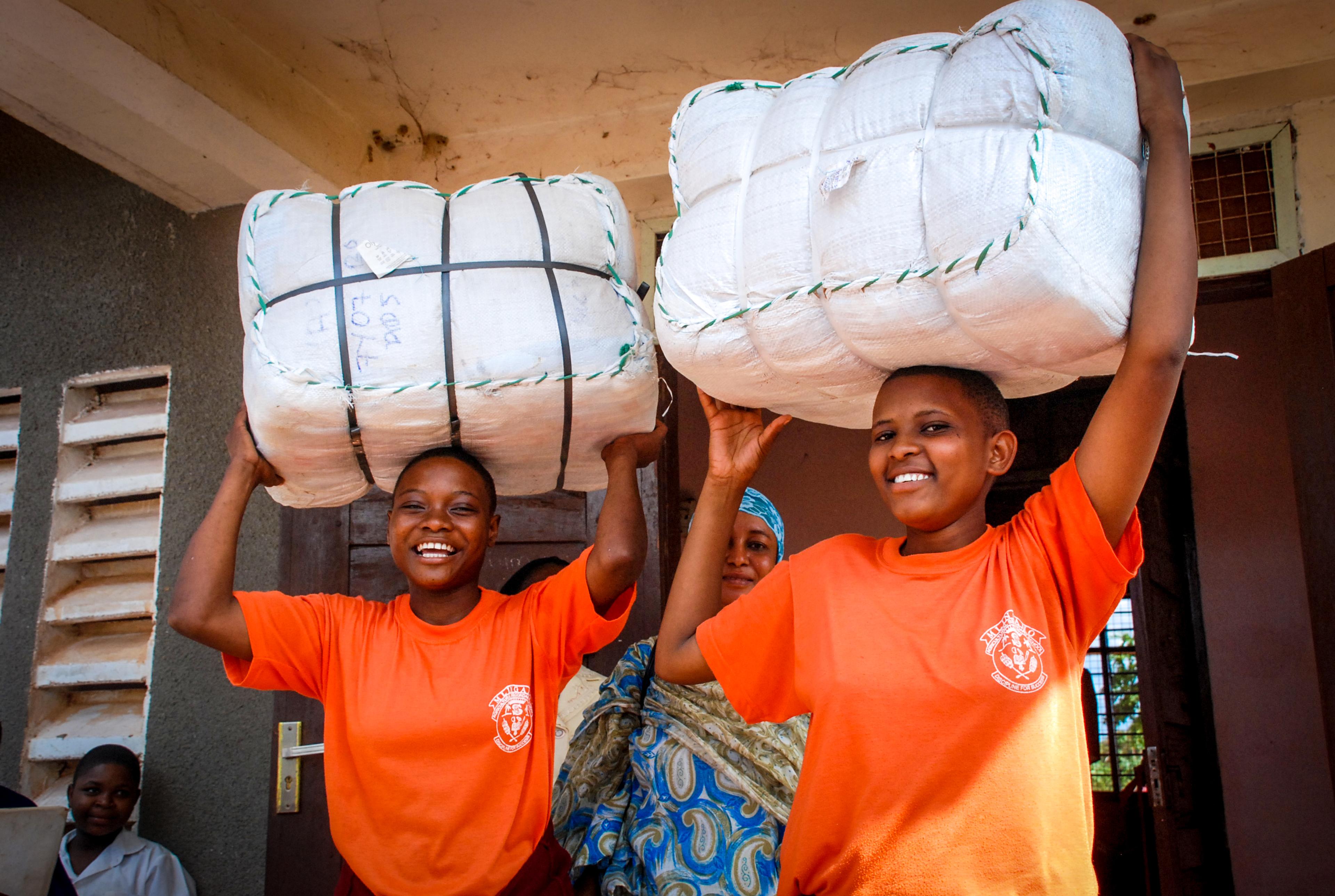 Women in Uganda holding bales of insecticide-treated bednets provided by the Against Malaria Foundation, one of Giving What We Can's Top Charities.