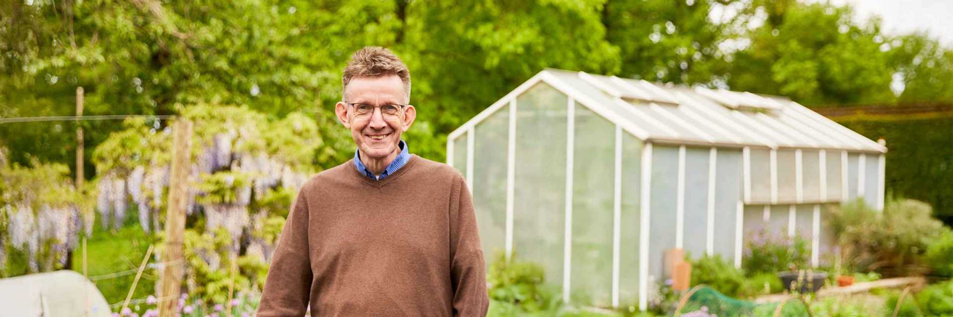 Gartenexperte Werner Peitzmann im Garten neben einem Hochbeet, im Hintergrund ein Gewächshaus