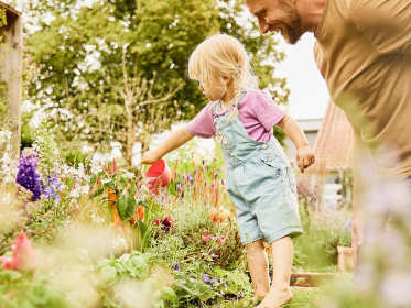Kleinkind gießt Blumen im Garten