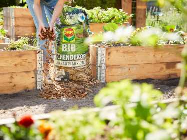 Frau füllt die Wege zwischen Hochbeeten mit COMPO BIO Eichendekor