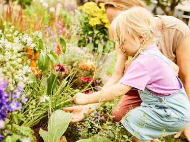 Kleines Mädchen und ihre Mutter entdecken eine Schneck im Garten