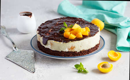 Cream mousse cake or no baked cheesecake with apricot decorated with chocolate, fresh apricots and mint on light background.