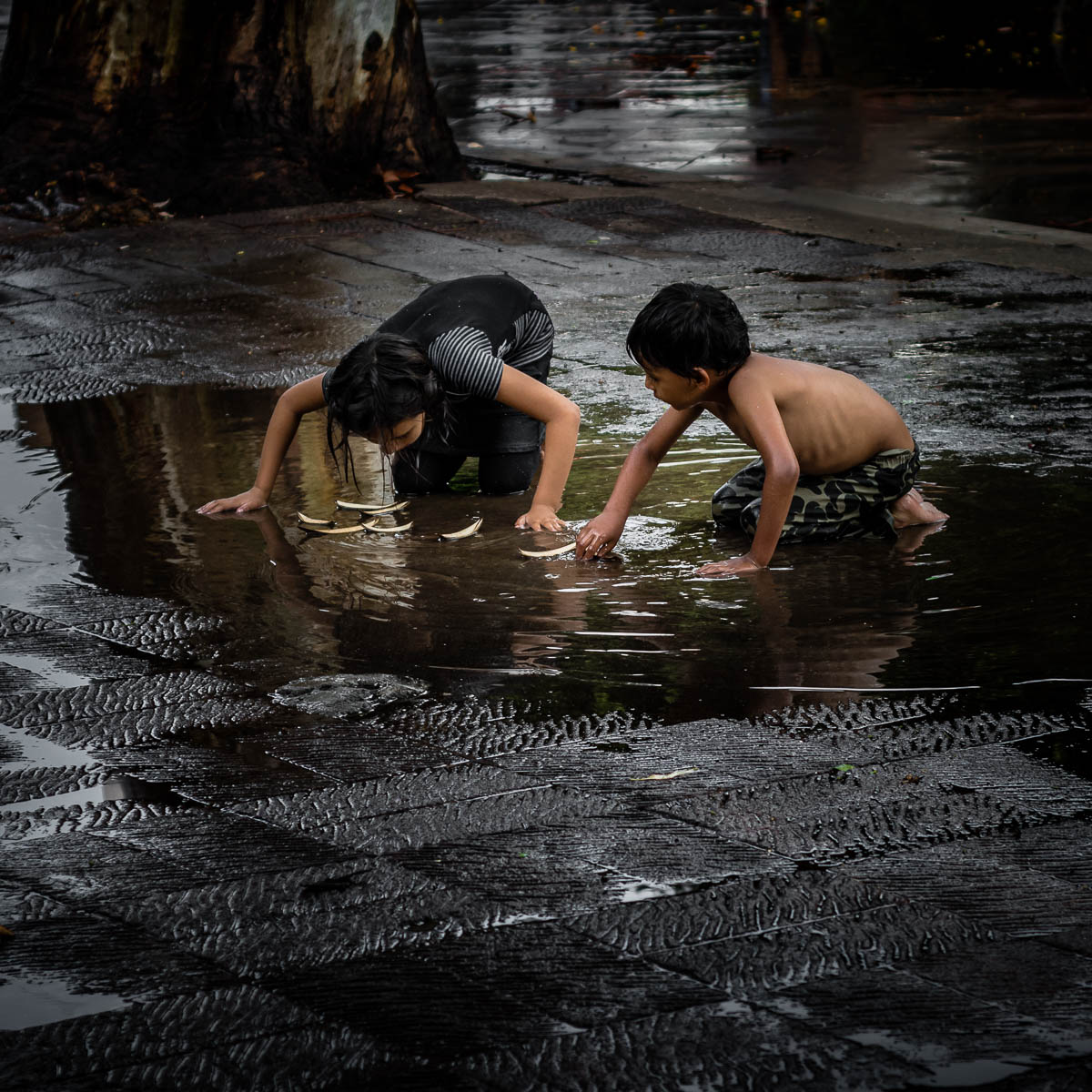 A brother and sister improvise and play in a puddle with boats they made out of fallen leaves after a brief afternoon thunderstorm hit the plaza in Ajijic, Mexico. One of the qualities that separates many kids who live in a place like the United States from, say, a place like Mexico is the ability, and at times the necessity, of creating games out of practical everyday items or found objects, such as pesos, rocks or these leaf boats, as shown in the photo.