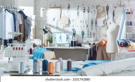 Shot of a Sunny Fashion Design Studio. We See Working Personal Computer, Hanging Clothes, Sewing Machine and Various Sewing Related Items on the Table, Mannequins Standing, Colorful Fabrics.