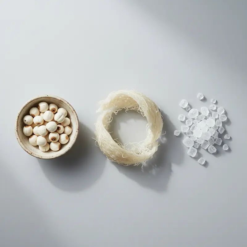 Các nguyên liệu chính để chưng yến hạt sen: tổ yến khô, hạt sen và đường phèn được bày trên nền đá xám.