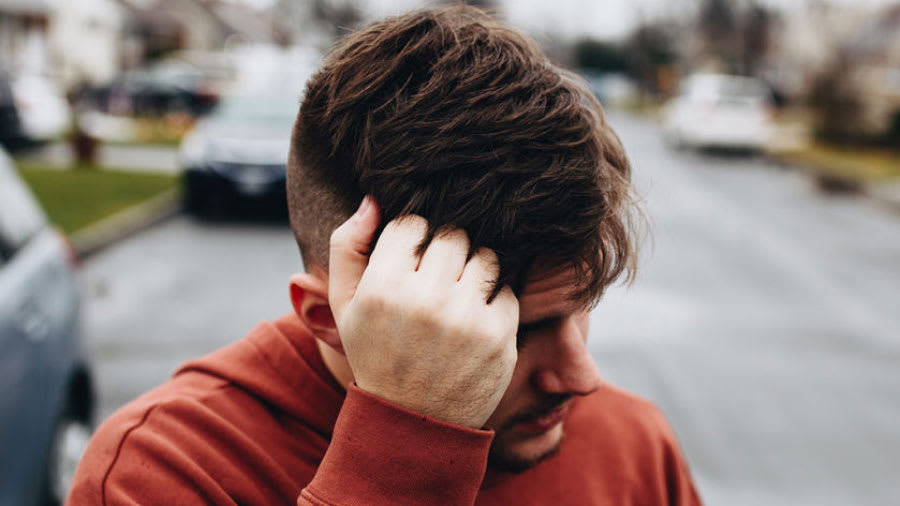 Man with low fade haircut wearing red crewneck sweater scratching head