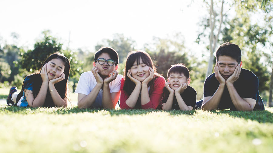 asian family laying on grass making silly funny faces​