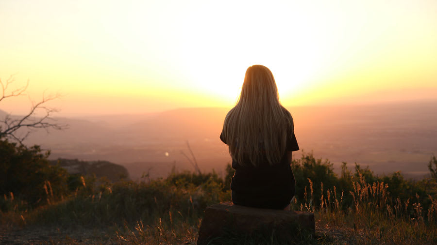 ​Woman looking over a city from hill with sunset over hills