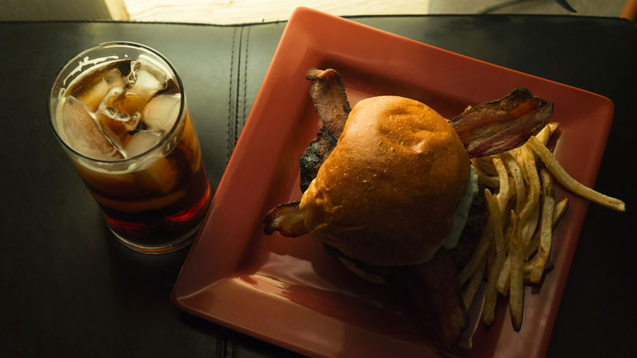 Bacon hamburger with french fries on a red square plate and a glass of whiskey on a leather seat