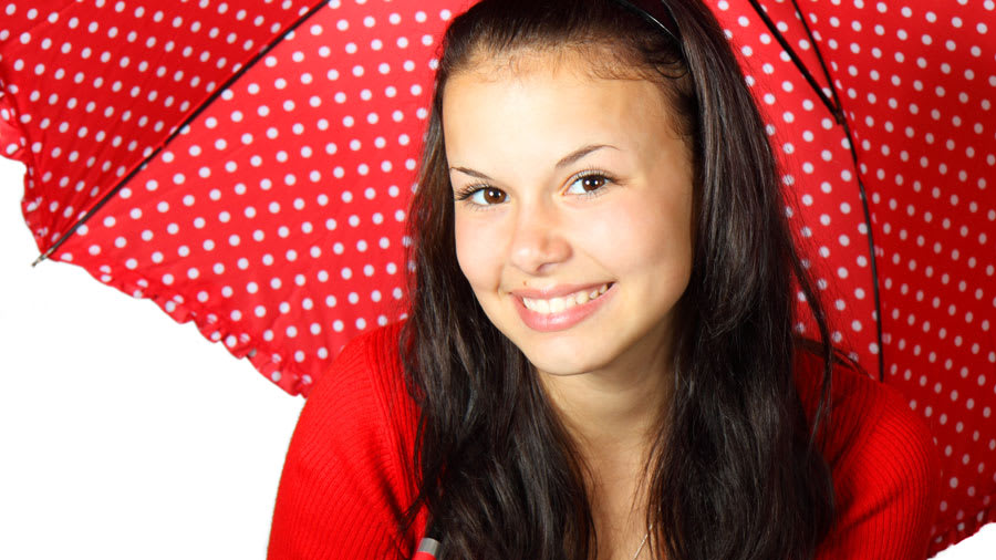 Brunette woman wearing a red shirt and holding a red umbrella with white polka dots