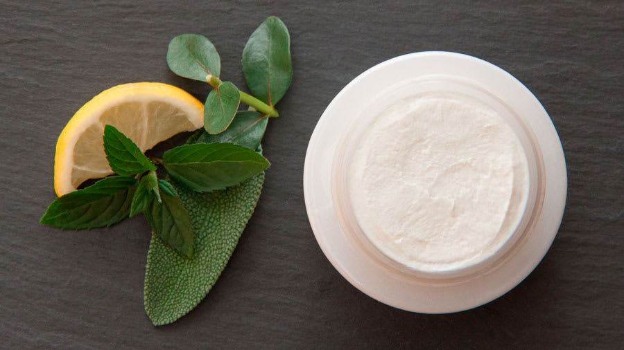 Lemon with some leaves next to top view of skin cream on a wooden table