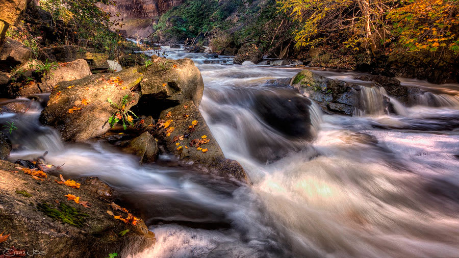 ​Stream water flowing over rocks with sunshine on one of the rocks