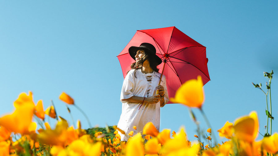Woman holding red umbrella outside on sunny day with orange flowers on the ground