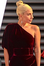 A picture of Lady Gaga in a burgundy one shoulder dress, looking to the right.