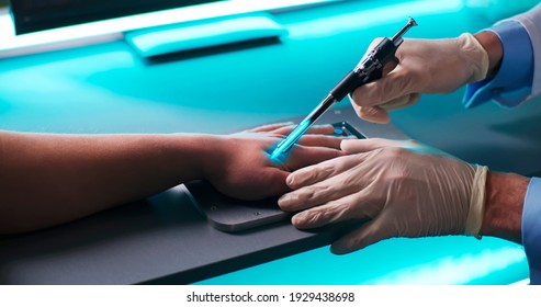 High angle of anonymous medical practitioner in gloves using modern tool to implant blue RFID microchip into hand of patient over table with futuristic scanner in laboratory