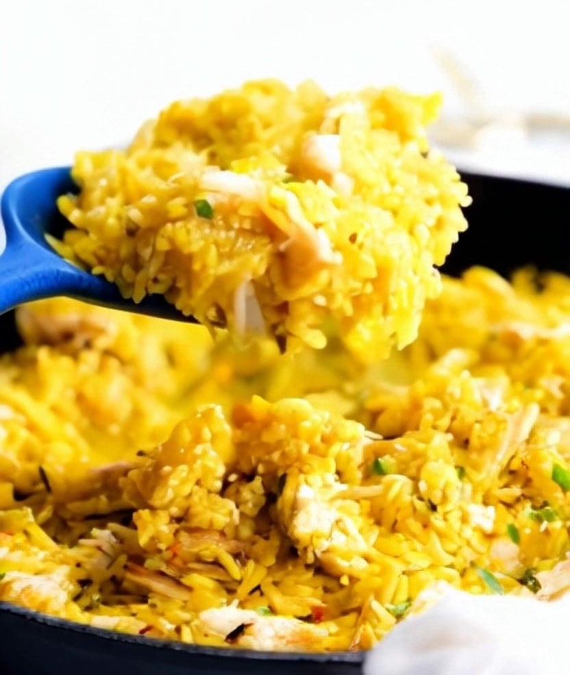 chicken and yellow rice in a pan with a blue spoon